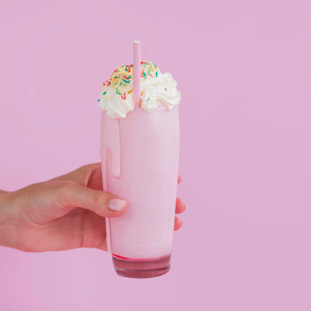 Pink milkshake with whipped cream and sprinkles held in hand